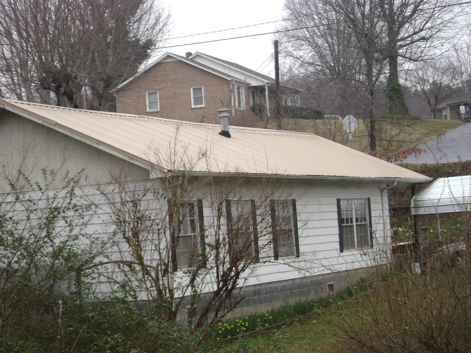 Tan metal roof on a white sided house set into a hillside — Commercial Roofing by Roofing Brothers in Lawnside